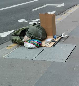 Homeless person sleeping on the street blocking the wind using a paper box.