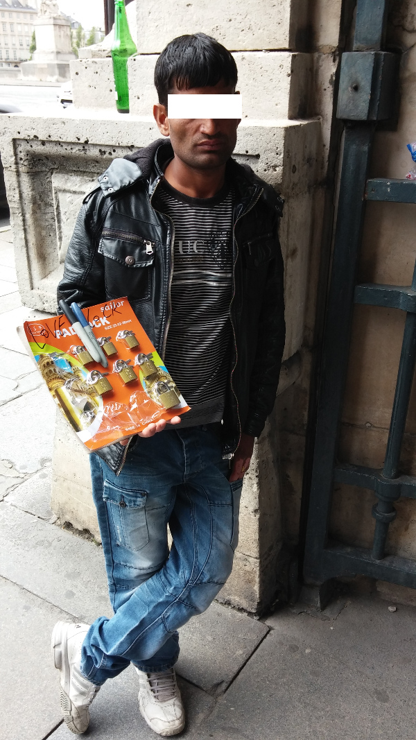 Bored-looking man carrying a package of welded locks with 'Love Lock' hand-written on it, who sells them for 1 Euro.