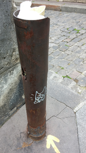 Rusty post with holes and some strange sort of cat face painted on it (vandalism)